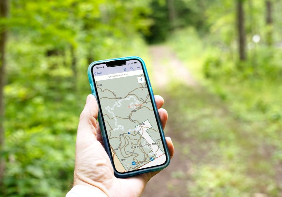 A hand holds a mobile phone with the Ganaraska Forest Trails Map on the screen