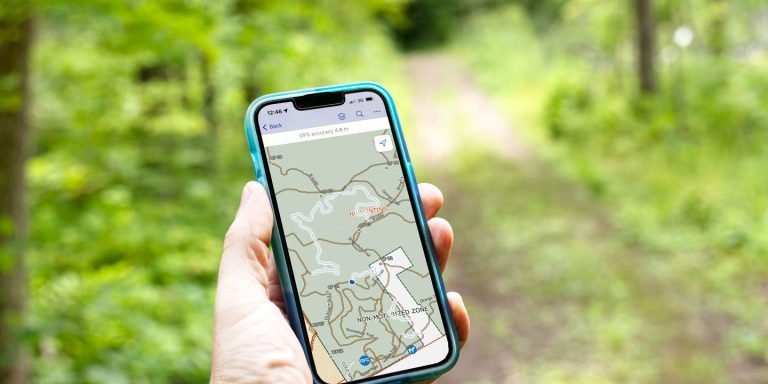 A hand holds a mobile phone with the Ganaraska Forest Trails Map on the screen